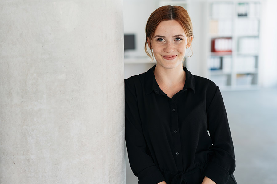 young businesswoman leaning against an interior office wall smiling