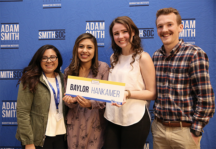 Four Baylor students from the Adam Smith Society holding a Baylor Hankamer sign