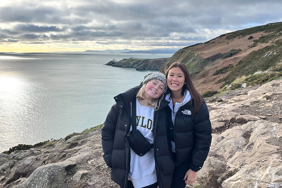 Two young college-aged women standing and smiling on a Dublin cliffside
