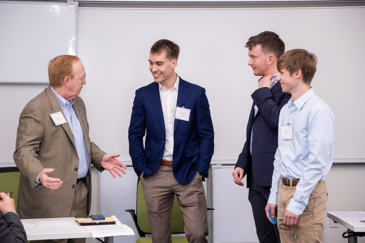 Three male students talking to a male instructor during the New Venture Competition