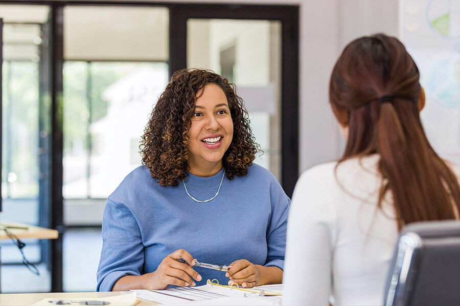 A woman sitting a table talking to another woman