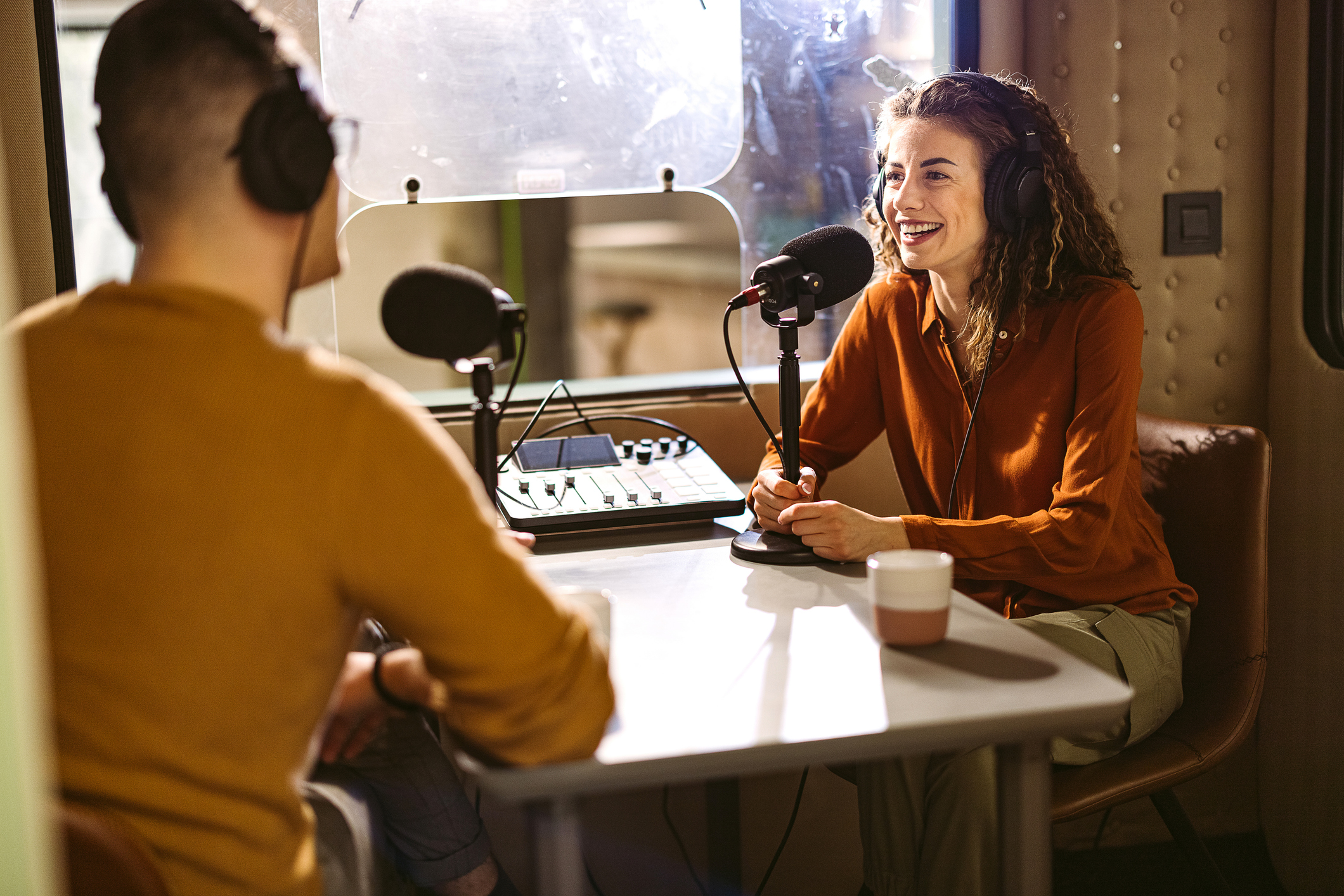 Two individuals recording a podcast with two mics, two headphones, in a booth
