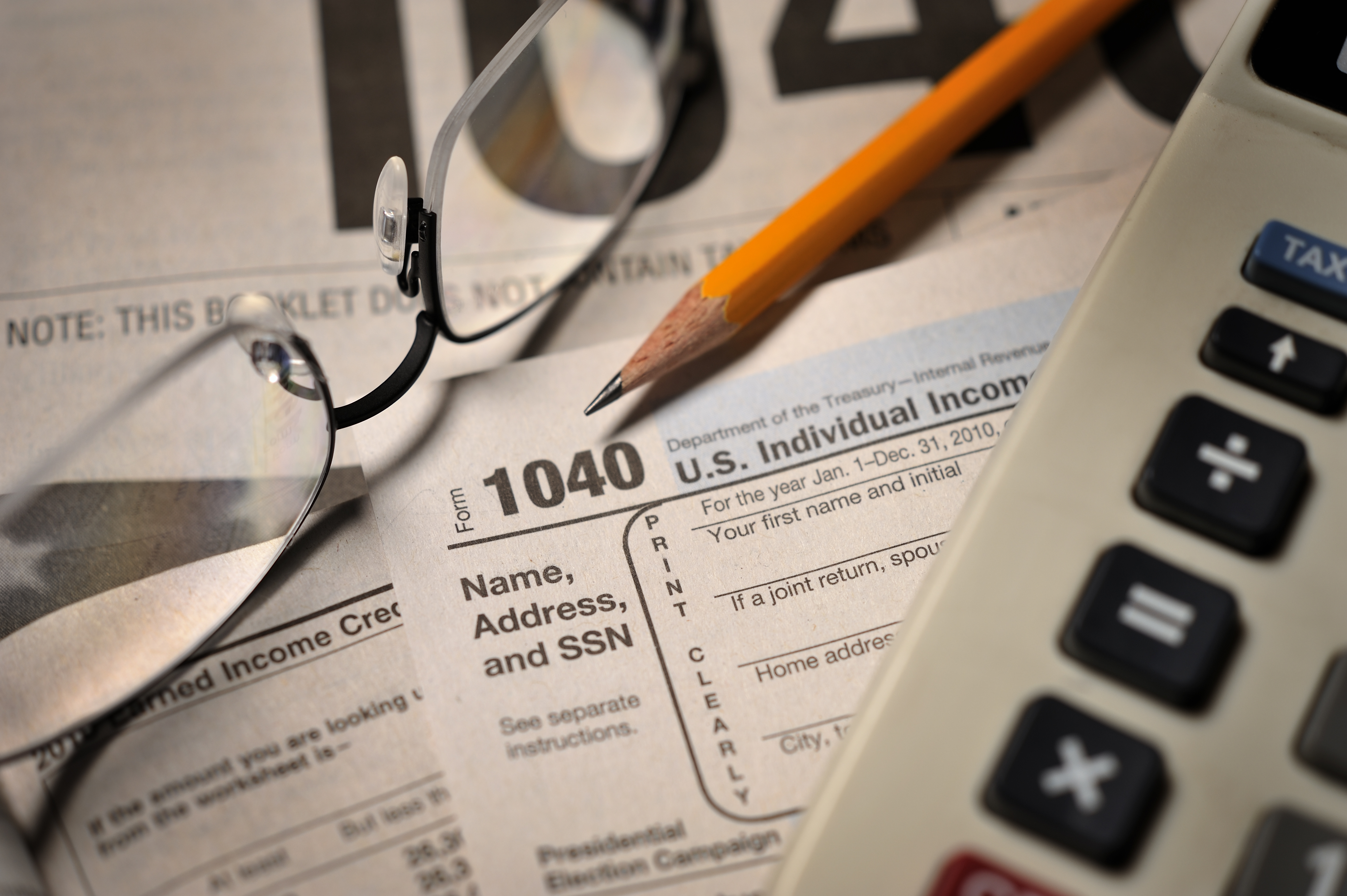 Calculator, glasses, and pencil on top of a tax form