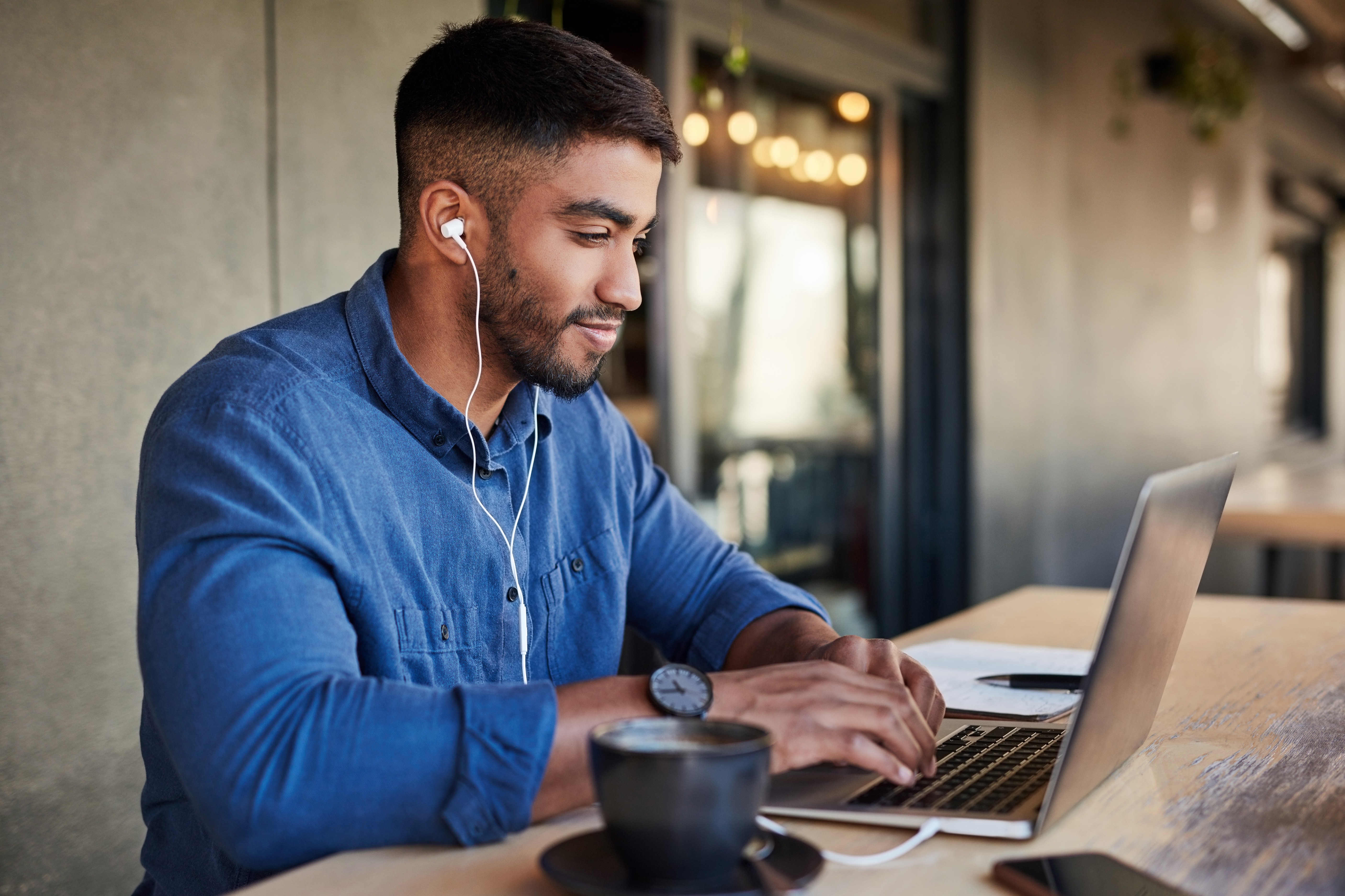 Professional man with earbuds and a laptop in a coffee shop