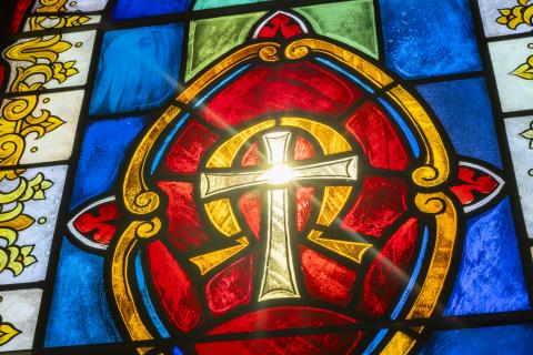 Stained glass of Cross and Omega symbol behind it with red and blue background glass