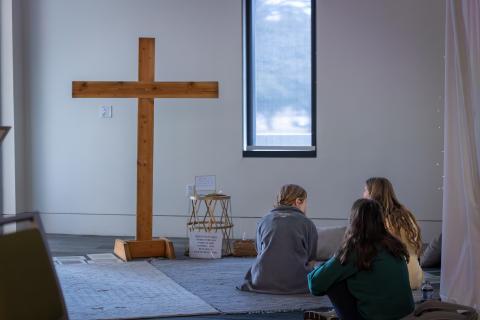 Room with a wooden cross and three female students on the floor praying together
