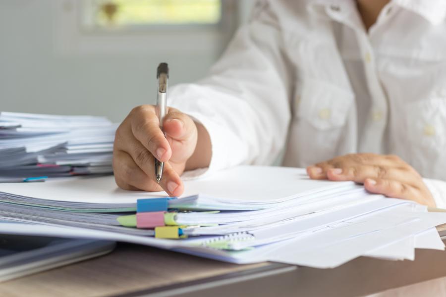 Woman seated with stacks of papers and holding a pen