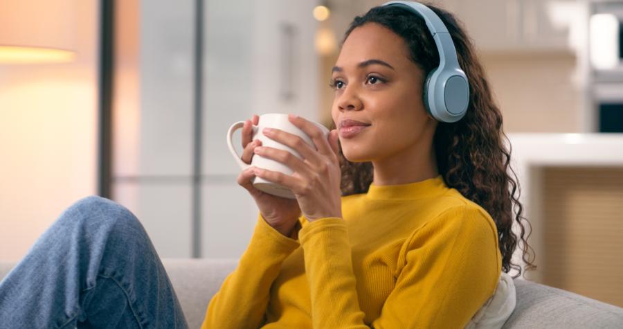Young woman listening to podcast with headphones holding a mug of coffee