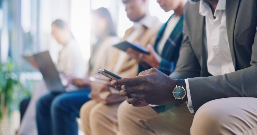 Business professionals seated in a row each looking at a digital device