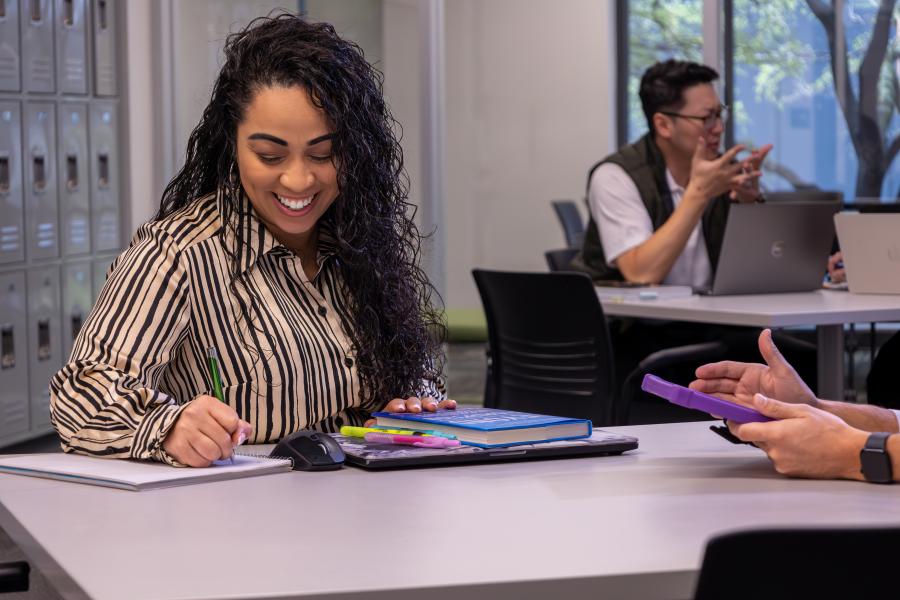 Female Baylor MBA student smiling at her desk in class writing with a pencil